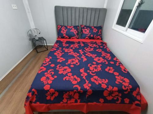 a bed with a blue bedspread with red flowers on it at KF Logement Wallis in Hihifo Airport