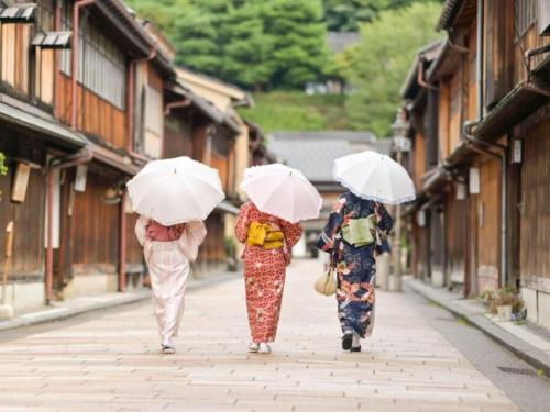 three women walking down a street holding umbrellas at Private Hotel Kanazawa SHIKI in Kanazawa