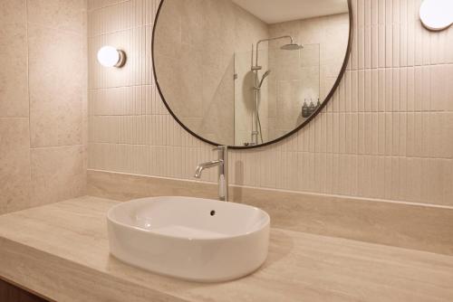 a bathroom with a sink and a round mirror at Flagstaff Gardens Hotel Melbourne in Melbourne
