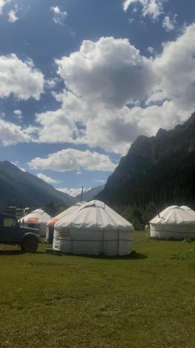 two large white tents in a field with mountains at Alim yurt camp in Mineralʼnyy Istochnik Altyn-Arasan