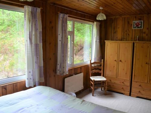a bedroom with a bed and two windows and a chair at Faichemard Farm Chalets in Invergarry