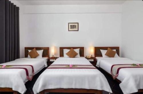 a room with three beds with white sheets and brown pillows at Khemra Guesthouse in Kampot in Kampot