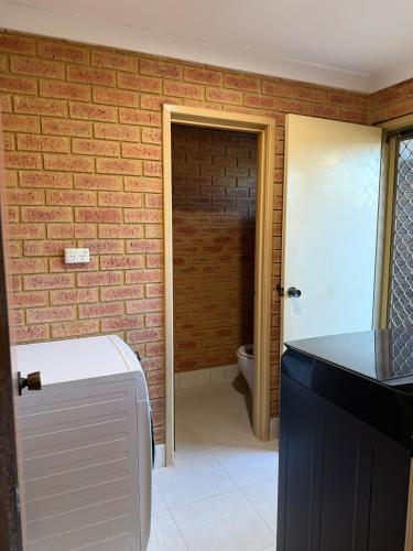 a bathroom with a toilet and a brick wall at Corner unit in Geraldton in Geraldton
