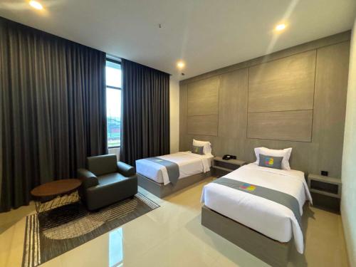 a hotel room with two beds and a chair at The Quadrant Hotel Ocarina Batam in Batam Center
