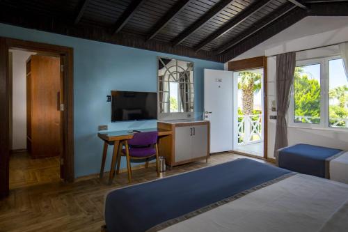 a bedroom with a bed and a desk and a tv at Adella Beach Resort Hotel in Kuşadası