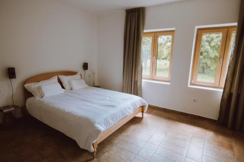 a bedroom with a bed with white sheets and windows at Nizija in Sombor