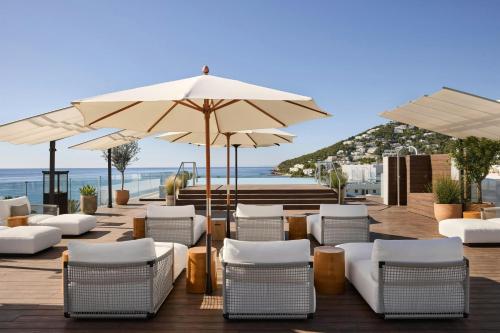 a patio with white chairs and umbrellas and the ocean at W Ibiza in Santa Eularia des Riu