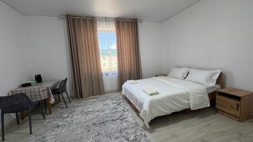 a bedroom with a bed and a table and a window at Guest House Alim in Karakol