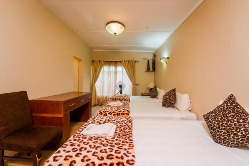 a hotel room with two beds and a desk at Guest Paradise Lodge in Victoria Falls