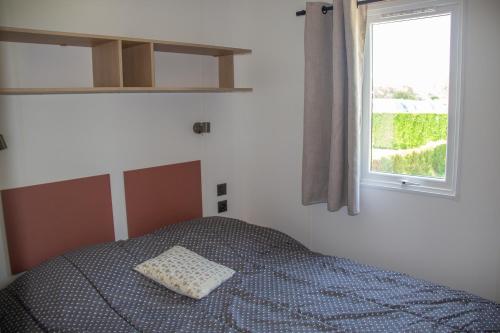 a bed with a pillow on it in a room with a window at Camping proche Bayeux et Omaha Beach in Tournières