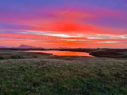 a sunset over a field with a body of water at Gramsdale House in Gramisdale