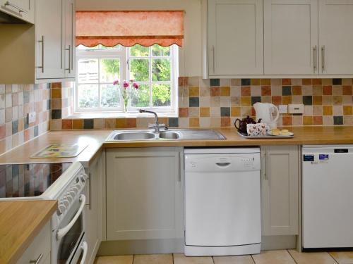 a white kitchen with a sink and a dishwasher at Churchill Cottage in Wootton Glanville
