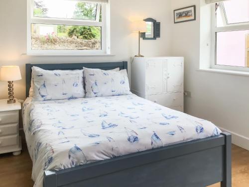 a bedroom with a bed with a blue comforter and two windows at Farthings - 19292 in Bridport
