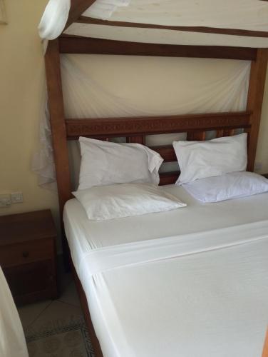 a bed with white sheets and pillows at Beach front Spacious Studio in Malindi