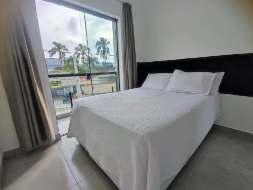 a bedroom with a white bed and a large window at Sobrado Matinhos 480 m da praia l novo l central 3quartos in Matinhos