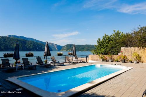 a swimming pool with chairs and umbrellas next to the water at Pensiunea Celestin in Eşelniţa