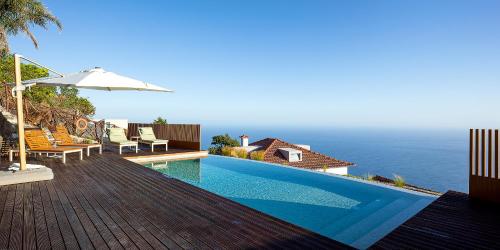 a swimming pool with an umbrella and the ocean at Massapez Royals in Fajã da Ovelha