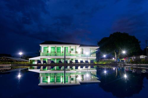 a white building with green doors on the water at night at Hotel Eden Parque del Cafe in Montenegro