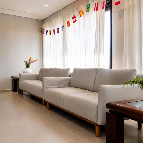 a living room with a white couch in front of a window at Hotel Mazzuco in Araranguá