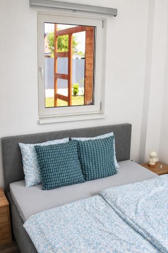 a bed with blue pillows sitting under a window at Fenyves Flow Apartman 1 in Balatonfenyves