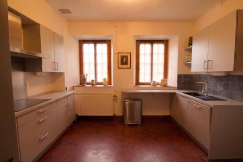 a kitchen with white cabinets and a sink and two windows at Gîte du Château de Spontin - 7a chaussée de Dinant - 5530 Spontin in Spontin