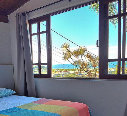 a bedroom with a window with a view of the ocean at Residencial Hibiscos - Vista Mar in Garopaba