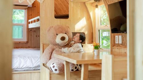 a little girl sitting at a table with a large teddy bear at Hongcheon Opera Bien Glamping in Hongcheon