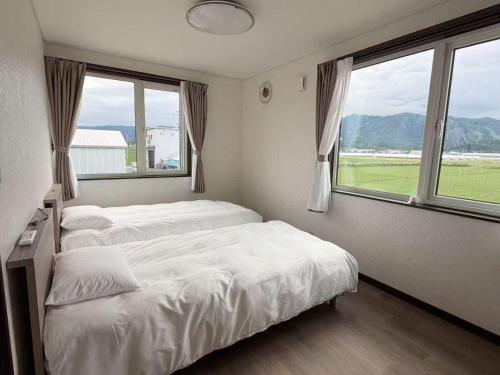 two beds in a room with two large windows at ゲストハウス 華園 in Furano