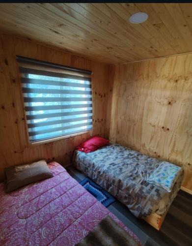 two beds in a wooden room with a window at Cabaña Rincón de Colbùn in Colbún
