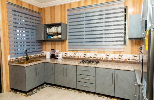 a kitchen with gray cabinets and a sink and windows at Edmundson Villa Apartment in Ejisu