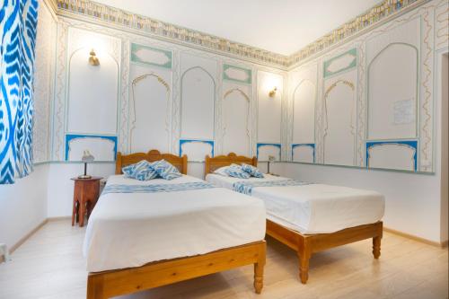 two beds in a room with blue and white wallpaper at Ismat Premium Guest House in Bukhara