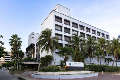 a white building with palm trees in front of it at Hotel Faranda Express Puerta Del Sol Barranquilla, A Member of Radisson Individuals in Barranquilla