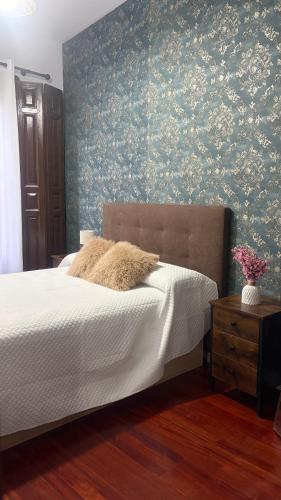 a bedroom with a bed and a wall with floral wallpaper at Un Rincón en Alcalá in Alcalá de Henares