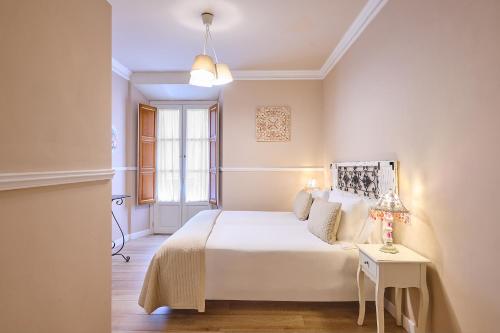 a white bedroom with a bed and a table at Apartamentos Luna Suites Palacio Almagra in Granada