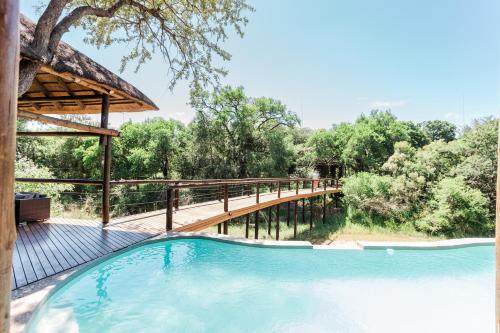 a bridge over a swimming pool next to a forest at Moditlo River Lodge in Hoedspruit