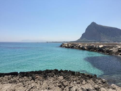 a beach with blue water and rocks and a mountain at Room 86 in San Vito lo Capo