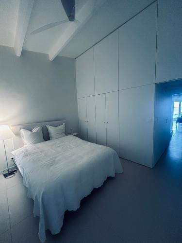 a white bedroom with a white bed and a lamp at L’Ile Rousse les pieds dans l’eau in LʼÎle-Rousse
