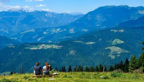 two people sitting on a bench looking at the mountains at Otta Apartments Golte in Mozirje