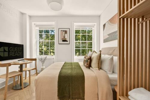 a bedroom with a bed and a desk and windows at GuestReady - The Crescent in London