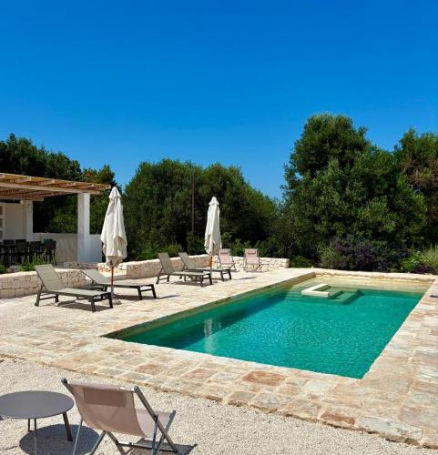 a swimming pool with chairs and umbrellas in a yard at Trullo botanico in Ceglie Messapica