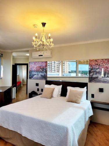 a bedroom with a large white bed and a chandelier at Hotel Itália in Paranavaí