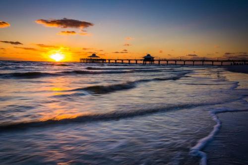 a beach with a pier and the ocean at sunset at Little EsCape in Matlacha