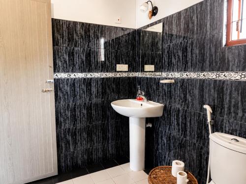 a black tiled bathroom with a sink and a toilet at Ceylon Glory Hostel in Negombo
