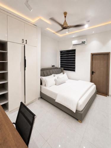 a white bedroom with a bed and a black chair at Maatambaba Homes in Tamale