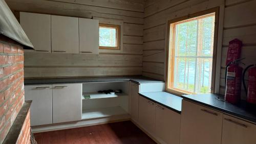 an empty kitchen with white cabinets and a window at Pitkälampi Private Lake Lodge in Jokikylä
