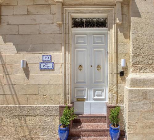 a white door on a stone building with two potted plants at Dar Vitorja in Senglea