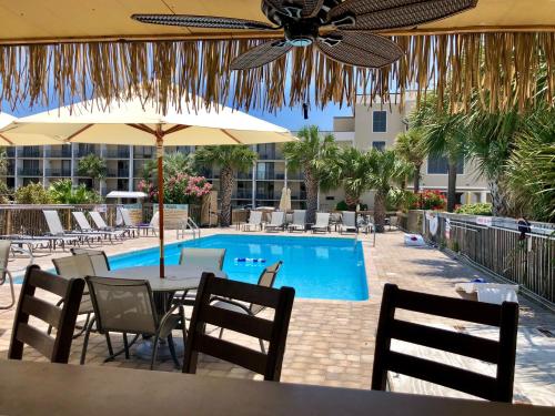 ein Pool mit Tisch, Stühlen und Sonnenschirm in der Unterkunft Hotel Tybee in Tybee Island