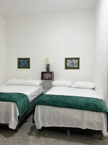 two beds in a white room with green sheets at Lu House in Flores