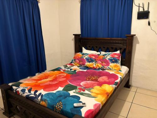 a bed with a floral comforter on it with blue curtains at Mapi's House in Paquera