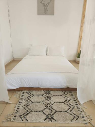 a bedroom with a white bed with a rug on the floor at קצה ההר in Amirim